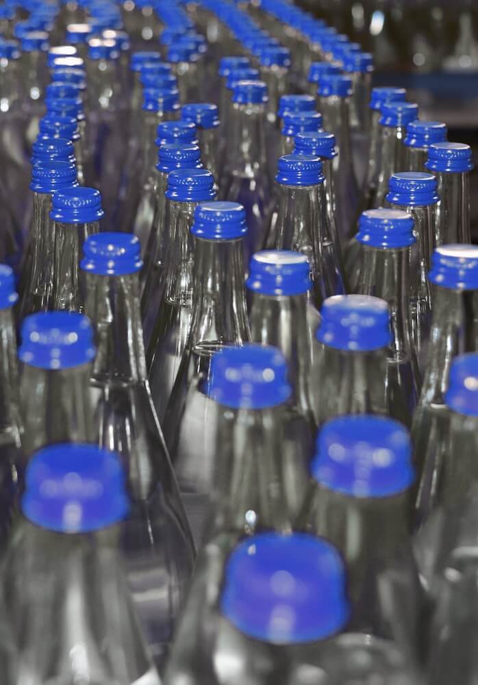 Nahaufnahme Glasflaschen mit blauem Deckel in Abfüllanlage